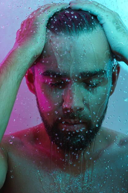 Bel homme sous l'écoulement de l'eau dans la lumière au néon