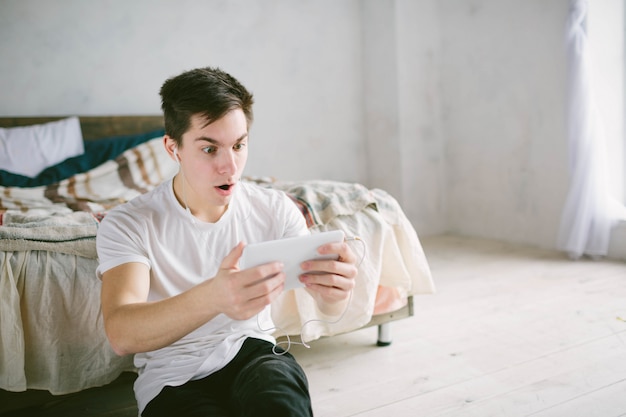 Bel homme surfant sur tablette. Guy parle avec des amis, vidéoconférence, skype, tablette. Le jeune étudiant fait défiler les réseaux sociaux