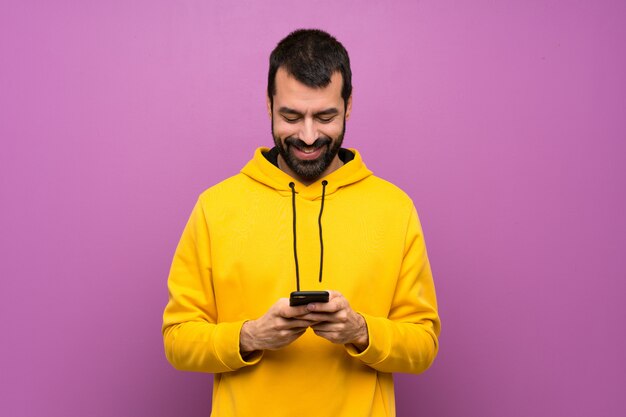 Bel homme avec un sweat-shirt jaune envoie un message avec le téléphone portable