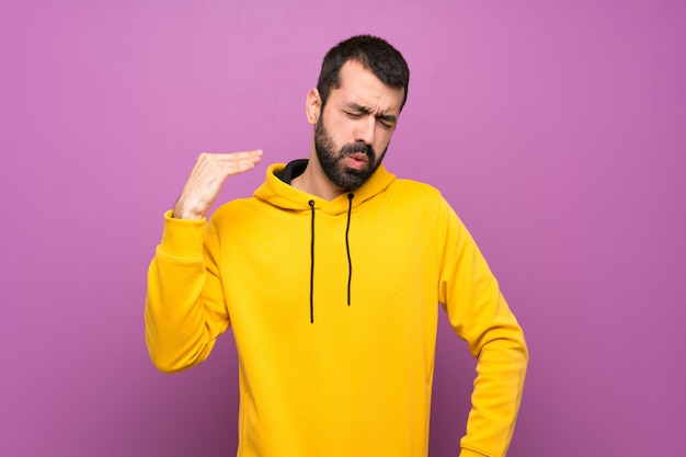 Bel homme avec un sweat-shirt jaune avec une expression fatiguée et malade