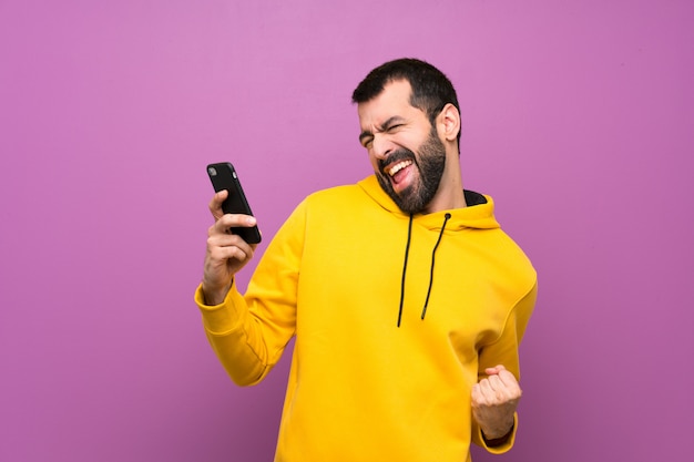 Bel homme avec un sweat-shirt jaune avec téléphone en position de victoire