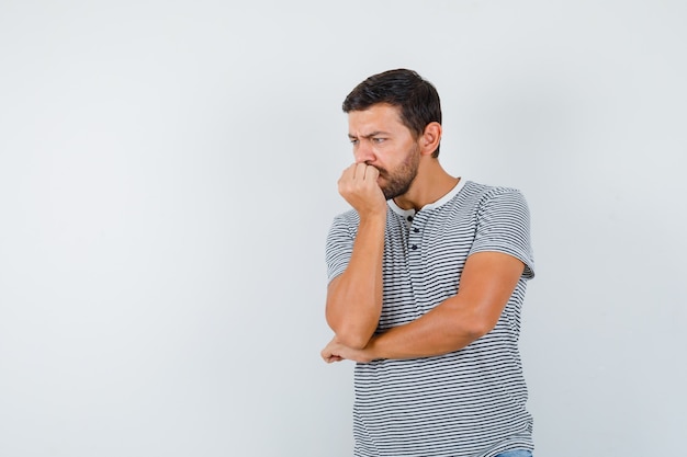 Bel homme en t-shirt se rongeant les ongles et ayant l'air mal à l'aise, vue de face.