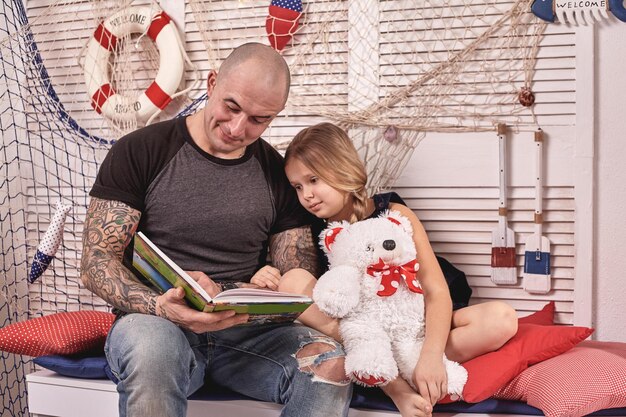 Photo un bel homme tatoué passe du temps avec sa petite fille mignonne à lire des contes de fées pendant que sa fille...