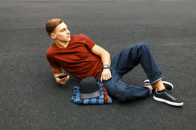 Bel homme avec téléphone allongé sur le trottoir et se repose.