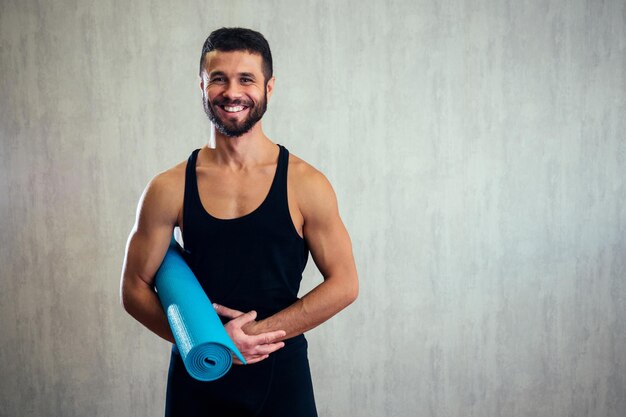 Bel homme tenant un tapis de yoga sur le sol. tapis de yoga bleu et instructeur d'étirement.