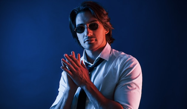Un bel homme en tenue de soirée et à lunettes est en studio avec un éclairage au néon bleu.