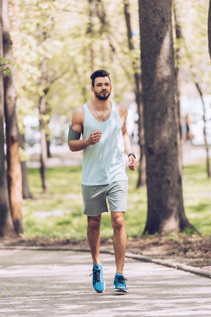 Photo bel homme en tenue de sport courant le long de la chaussée dans un parc verdoyant