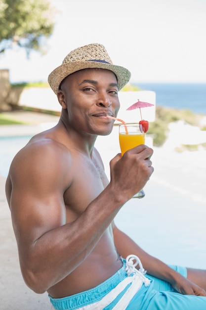 Bel homme torse nu relaxant avec cocktail au bord de la piscine