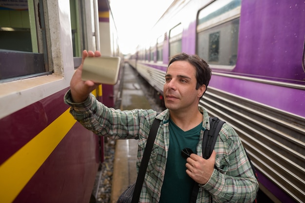 Bel homme de touriste persan à l'aide de téléphone à la gare