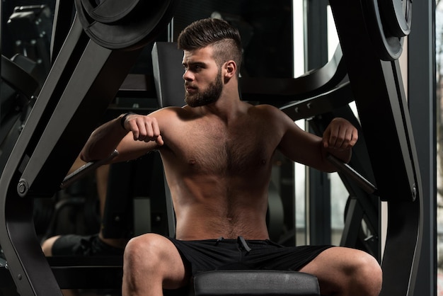 Bel homme travaille sur la poitrine sur la machine dans une salle de sport moderne