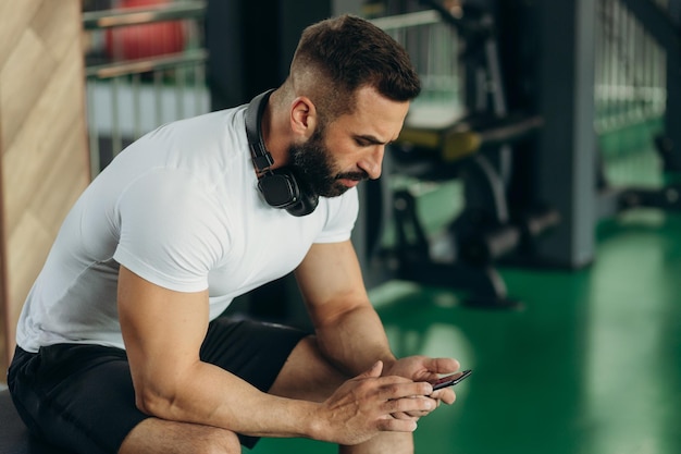 Bel homme utilisant le téléphone tout en faisant une pause d'exercice dans la salle de sport