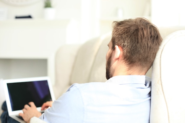 Bel Homme Utilise Une Tablette Numérique Et Sourit En Se Reposant Sur Un Canapé à La Maison.