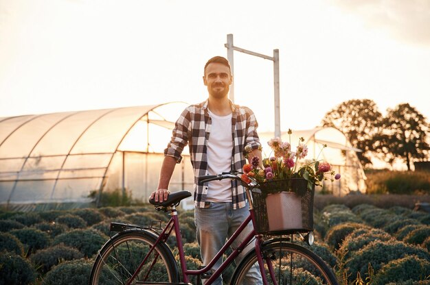 Photo un bel homme en vêtements décontractés est à vélo sur le champ agricole près de la serre