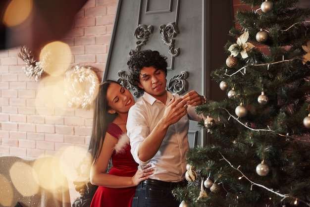 Bel intérieur. Couple romantique habillant l'arbre de Noël dans la chambre avec mur marron et cheminée.