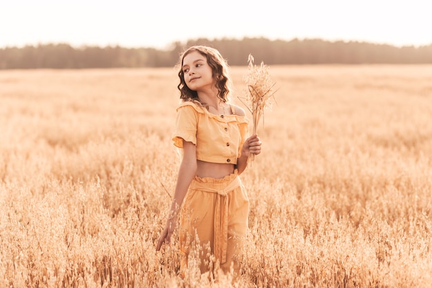 Belle adolescente aux cheveux longs marchant dans un champ de blé par une journée ensoleillée. Portrait à l'extérieur. Écolière relaxante