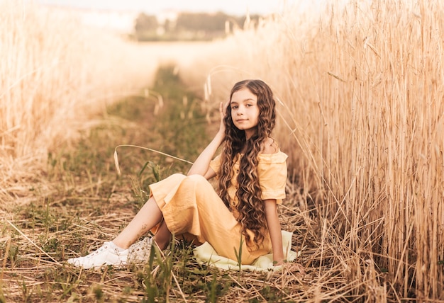 Belle adolescente aux cheveux longs marchant dans un champ de blé par une journée ensoleillée. Portrait à l'extérieur. Écolière relaxante