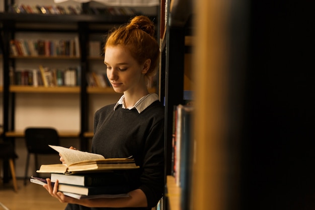 Belle adolescente aux cheveux rouges portant des livres à la bibliothèque