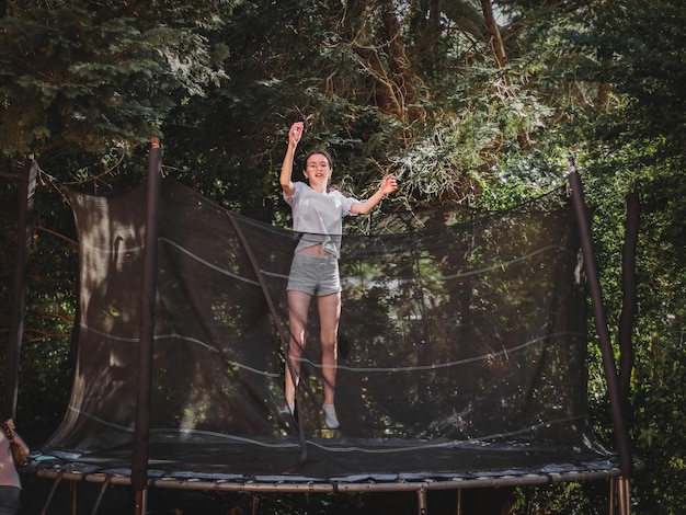 Une belle adolescente blanche et mince en short et en blouse saute sur un trampoline.