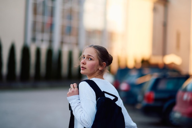 Une belle adolescente blonde rentre de l'école au coucher du soleil avec son sac à dos.