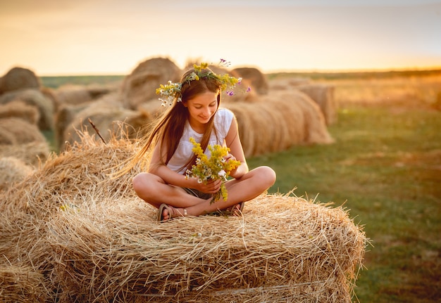 Belle adolescente avec bouquet floral, sur une botte de foin