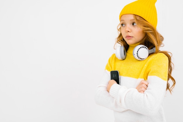 Belle adolescente caucasienne avec chapeau jaune, pantalon, t-shirt blanc et veste tient un gros sac à dos dans ses mains isolé sur blanc