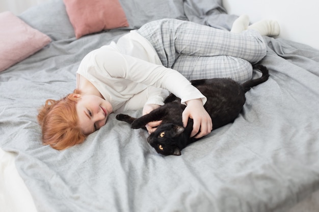 Belle adolescente avec chat noir sur lit à la maison