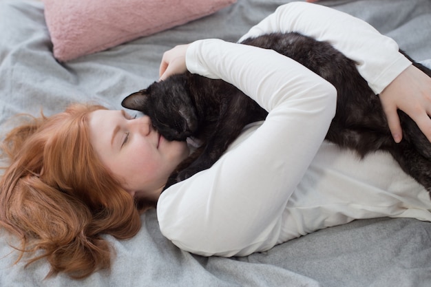 Belle adolescente avec chat noir sur lit à la maison