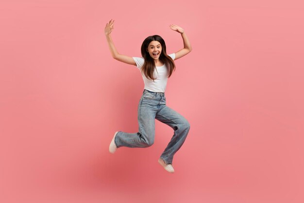 Une belle adolescente joyeuse sautant en l'air sur un fond de studio rose.