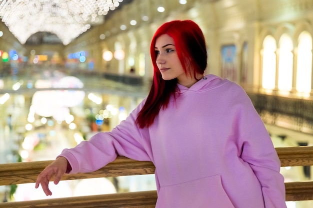 Belle adolescente rousse en sweat à capuche rose le soir dans la rue éclairée de la ville.