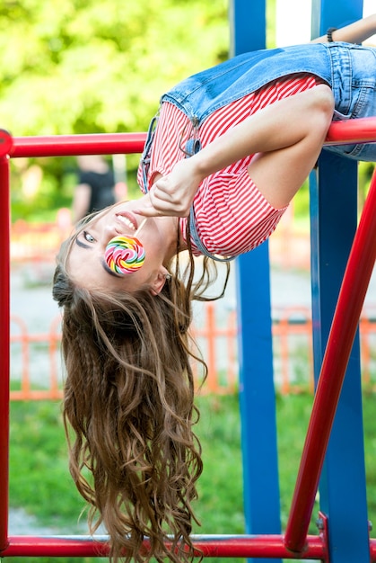 Belle adolescente en salopette en denim avec sucette à l'envers