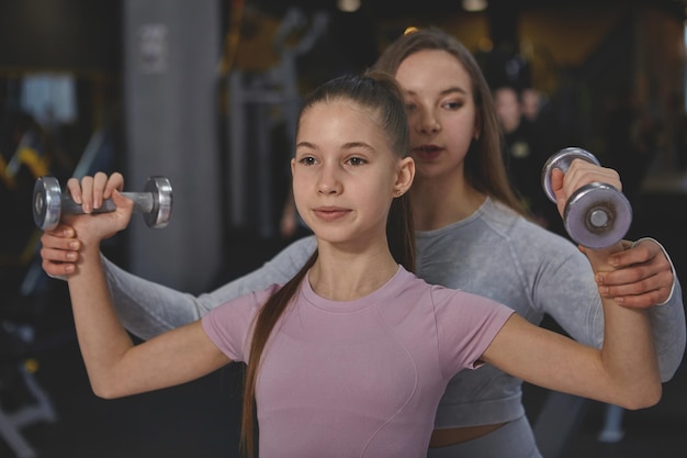 Belle adolescente soulevant des haltères faisant de l'exercice avec une athlète féminine professionnelle au gymnase