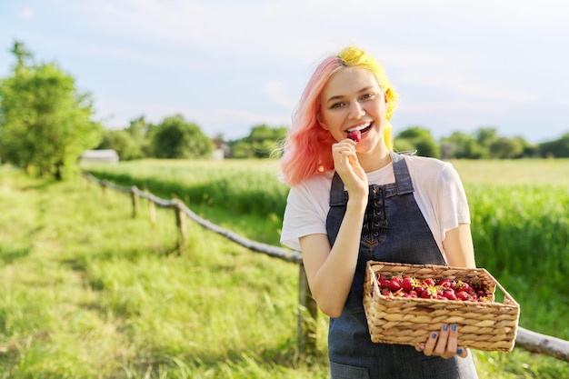 Belle adolescente souriante dans une ferme rustique avec panier de fraises fraîches copiez l'espace sur l'herbe verte