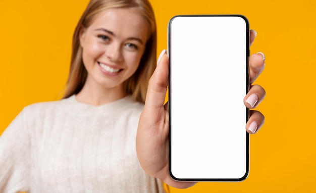 Belle adolescente souriante démontrant un smartphone avec un écran blanc vierge