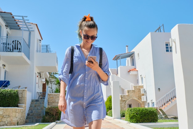 Belle adolescente souriante marchant à l'aide de smartphone