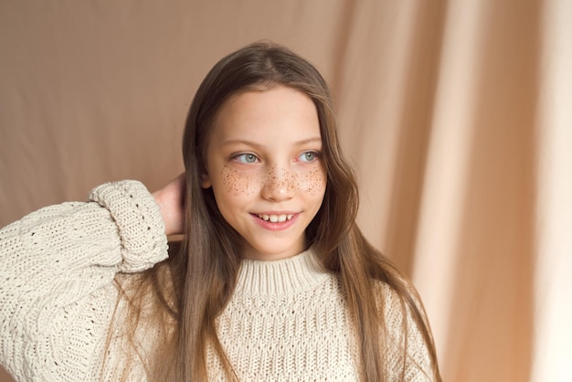 Belle adolescente avec des taches de rousseur dorées sur le visage posant sur fond beige