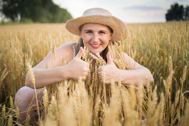 Une belle agricultrice d'âge moyen dans un chapeau de paille et une chemise à carreaux se tient dans un champ de blé mûrissant doré pendant la journée au soleil
