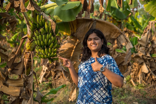 Belle agricultrice examine ou observe ou tient des bananes sur l'arbre dans une ferme biologique. Visage souriant d'un agriculteur avancé dans le domaine de la ferme agricole.