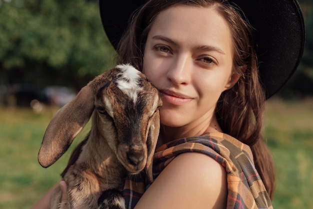 Belle agricultrice avec une petite chèvre à la campagne a de l'amitié dans la nature