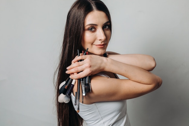 Belle artiste féminine avec des pinceaux de maquillage dans un salon de beauté sur un mur léger