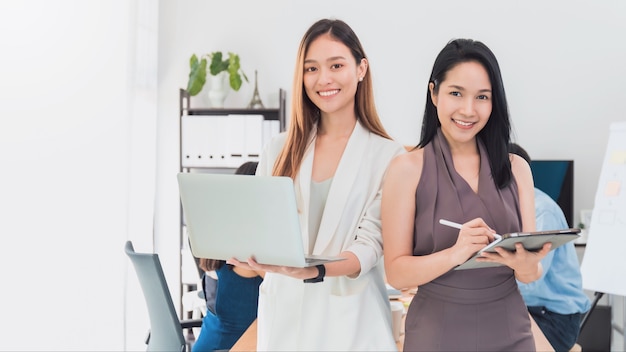 Belle asiatique femme habilitée tenant un ordinateur portable et une tablette avec un ami travaillant dans la salle de réunion au bureau. Propriétaire femme d'affaires démarrage avec confiance et gaieté.