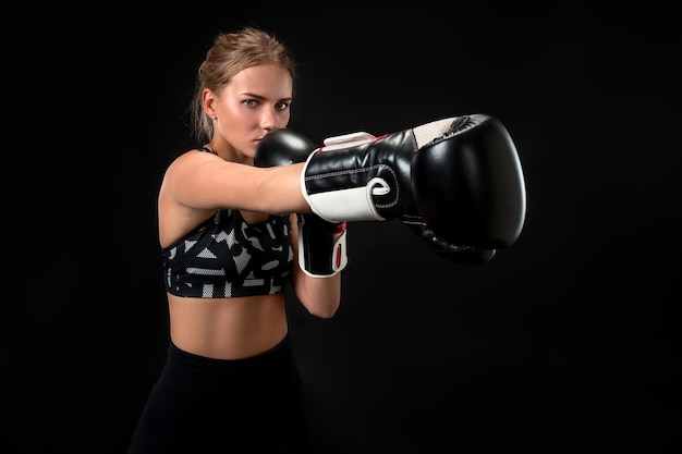 Belle athlète féminine en gants de boxe, en studio sur fond noir. Le boxeur accomplit le coup. Focus sur le gant