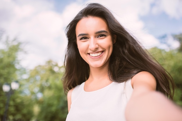 Belle autoportrait de jeune femme souriante brune sur fond nature et ciel dans le parc Travel Selfie Instagram