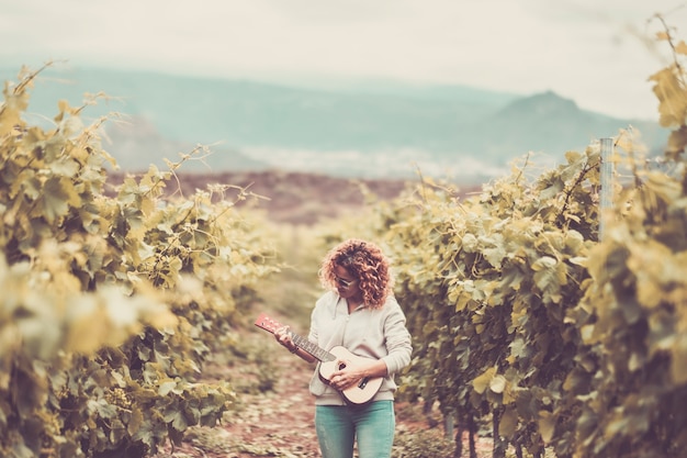 belle belle femme caucasienne marche seule dans le vignoble fond vert chantant une guitare acoustique ukulélé