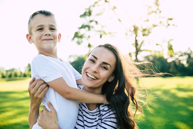 Belle belle jeune mère avec son petit fils mignon s'amuse et s'embrasse tout en se reposant sur l'herbe dans le parc à l'extérieur