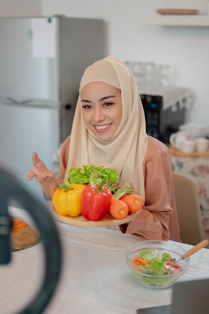 Une belle blogueuse musulmane asiatique en train d'enregistrer sa vidéo de cuisine dans la cuisine.