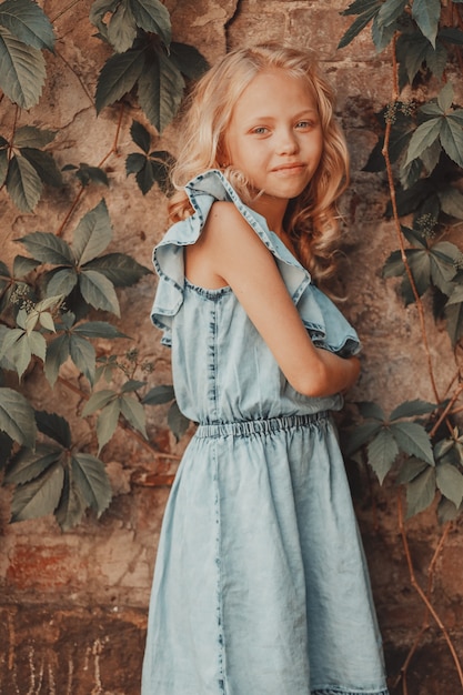 Belle blonde aux cheveux bouclés se tient contre le mur avec des feuilles de vigne sauvages. photo de haute qualité