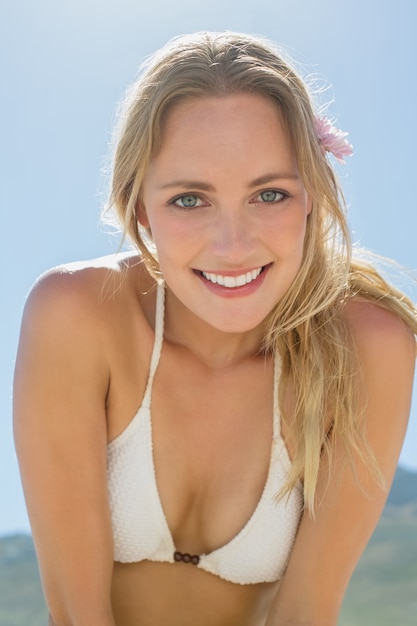 Belle blonde en bikini blanc, souriant à la caméra sur la plage