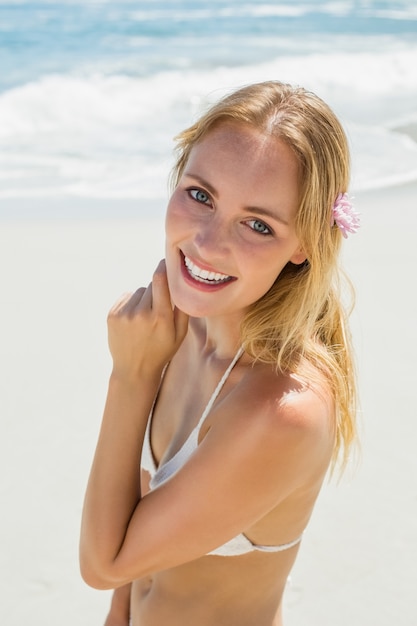 Belle blonde en bikini blanc, souriant à la caméra sur la plage