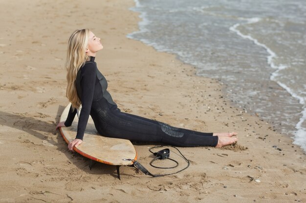 Belle blonde en combinaison avec planche de surf à la plage