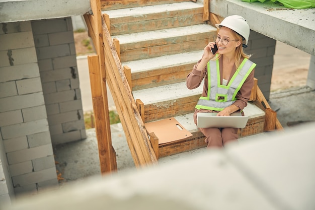 Belle Blonde Heureuse Ingénieur Civil Caucasien Dans Un Gilet Réfléchissant Ayant Une Conversation Téléphonique à L'extérieur